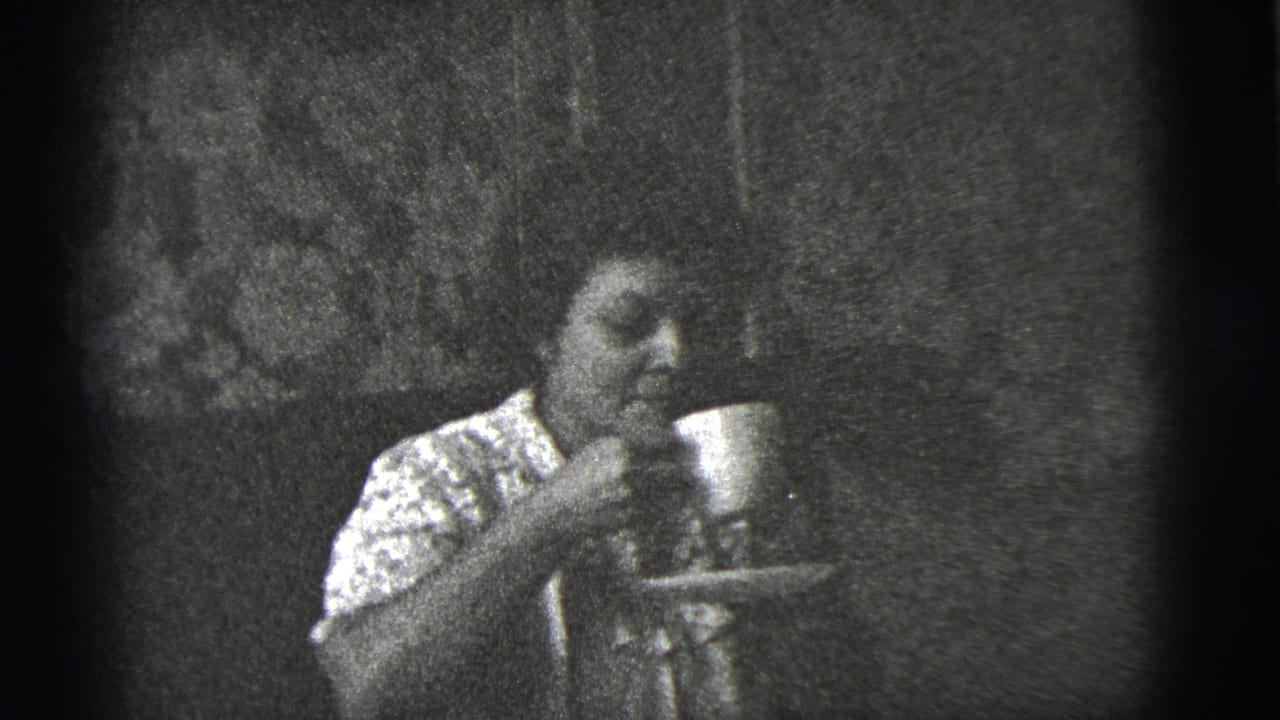 Woman in a patterned dress sits indoors holding a cup and saucer.