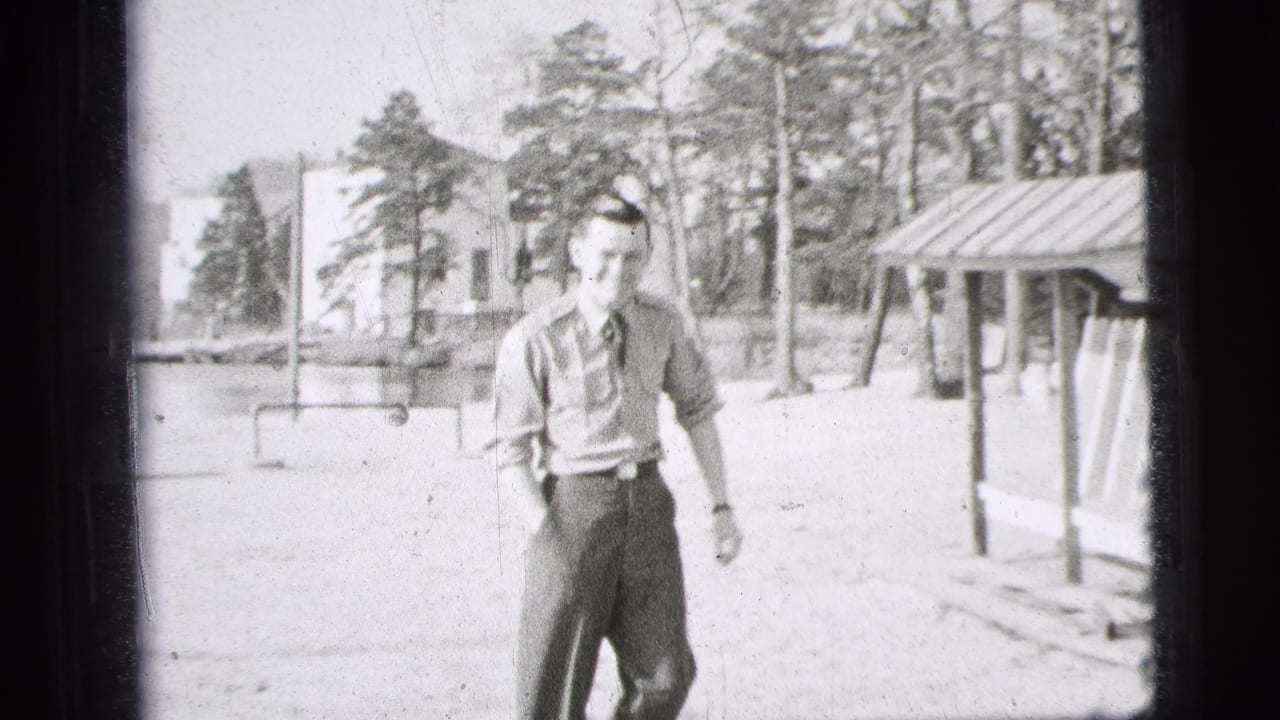 A young man in a short-sleeved military-style uniform walks toward the camera in bright outdoor 1956 New York City home-movie footage.