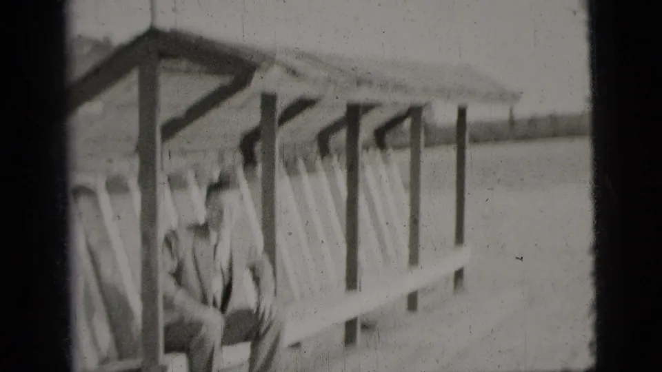 A closer, soft-focus view shows the man seated under the shelter, with the bench and diagonal supports filling much of the frame.