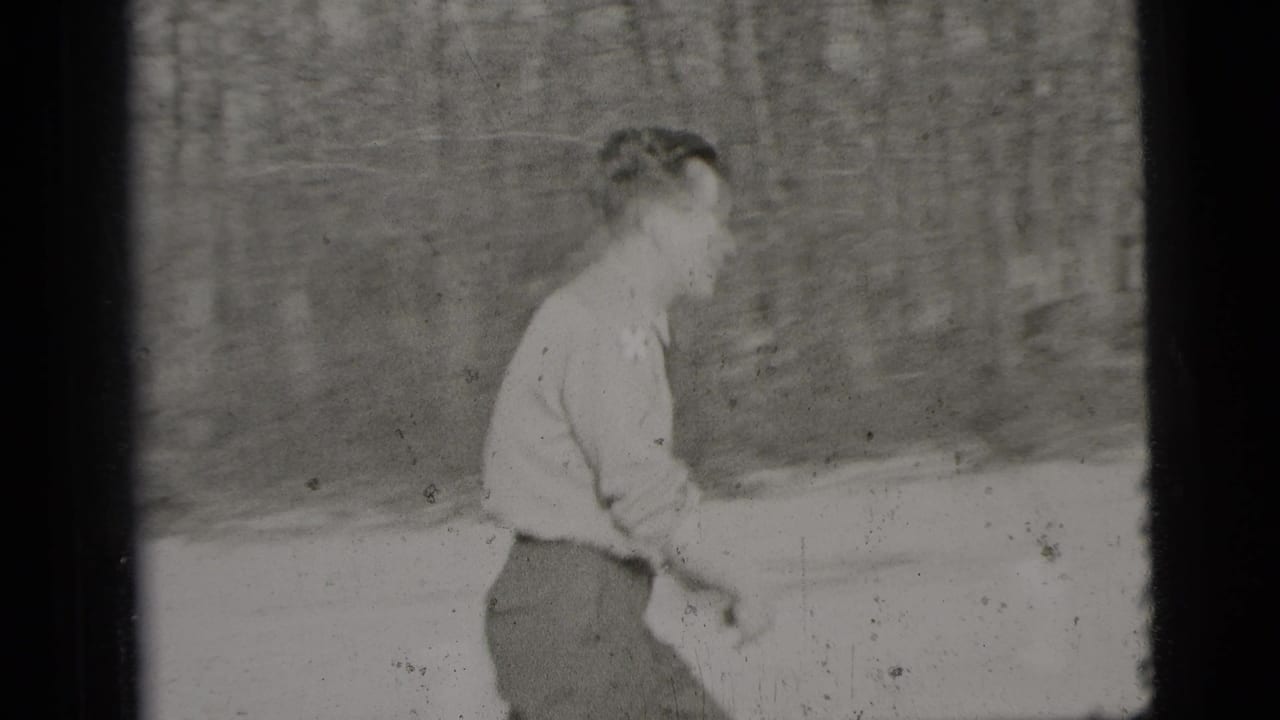 Man in a light shirt walking across sandy ground beside trees.