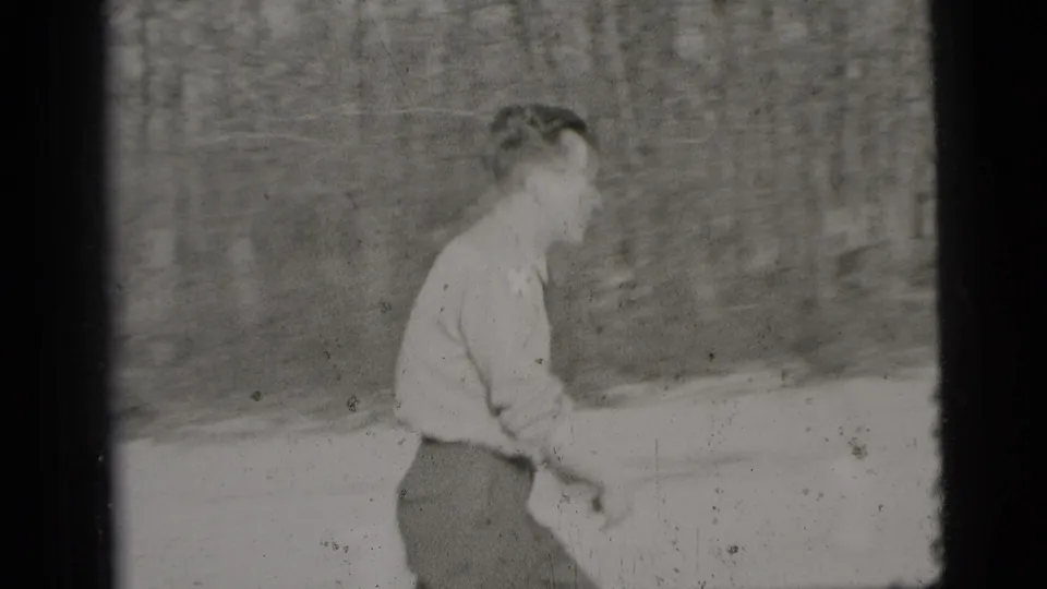 Adult man in a light shirt and dark trousers walks through a sandy outdoor area in 1956 New York City home-movie footage.