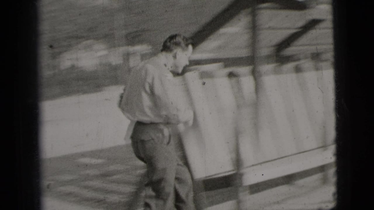 The man moves along a wooden slatted shelter or bench structure in a sandy outdoor recreation area.