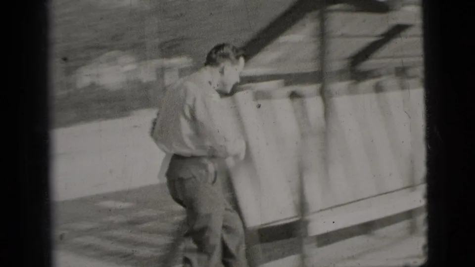 The man moves along a wooden slatted shelter or bench structure in a sandy outdoor recreation area.