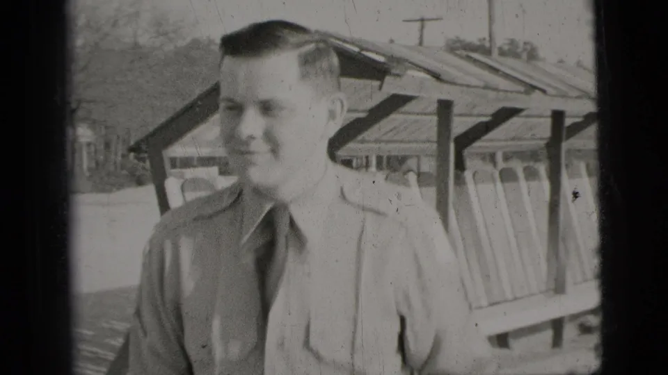 Closer 1956 New York City frame of the young man smiling in a light shirt and dark tie beside the shelter structure.