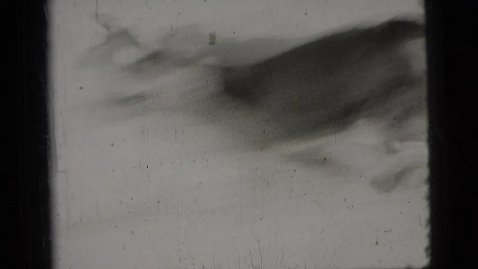 The dog is heavily motion-blurred while running across the pale surface in the black-and-white 8mm frame.