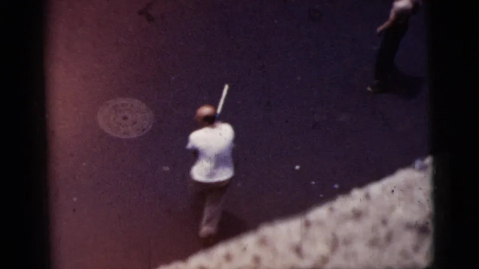 Home-movie frame from the same 1956 New York City clip showing people on pavement from above, with one figure holding a long light object.