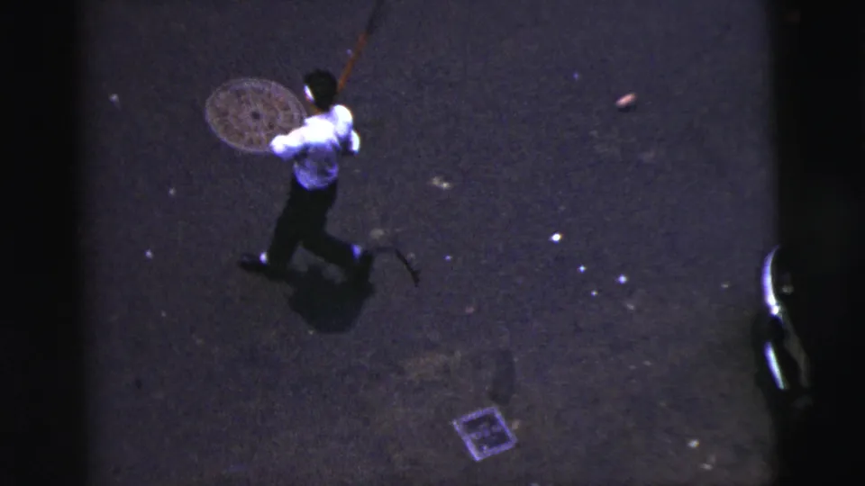 A man appears mid-swing or follow-through on a dark 1956 New York City street, seen from above.