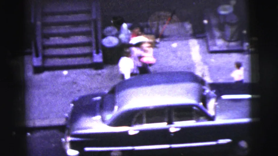 Elevated 1956 New York City street view with several people near a curb, steps, and a large parked car.
