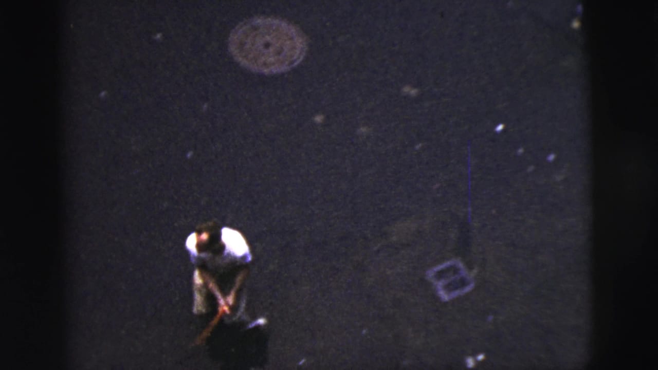 Adult man bends on a dark paved street near scattered marks and street debris.