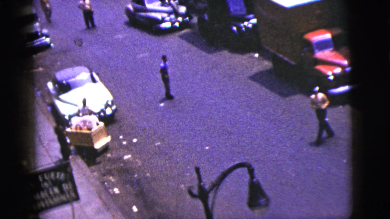 Elevated street view with parked cars, pedestrians, a pushcart, and a storefront sign.