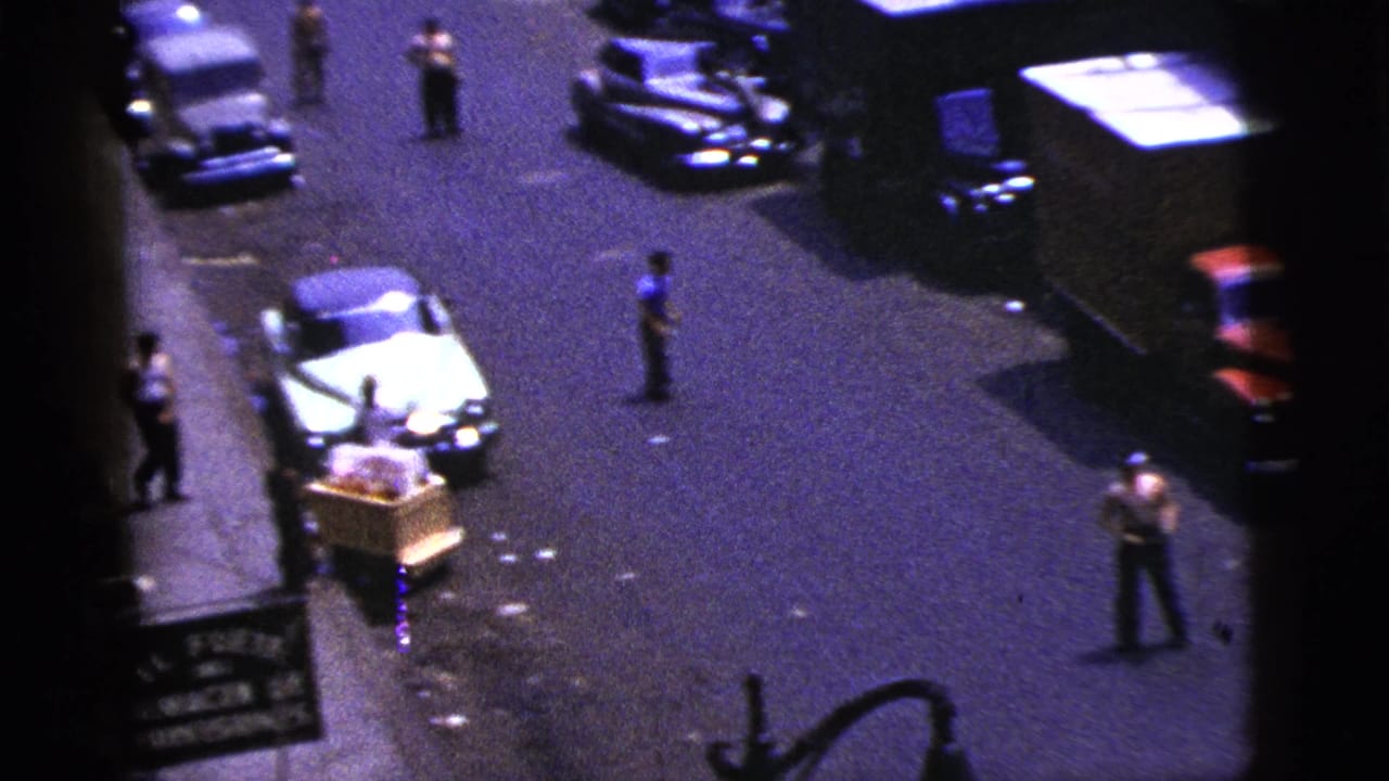 Elevated 1956 New York City street view with mid-century parked cars, pedestrians, sidewalk edges, and storefront frontage.