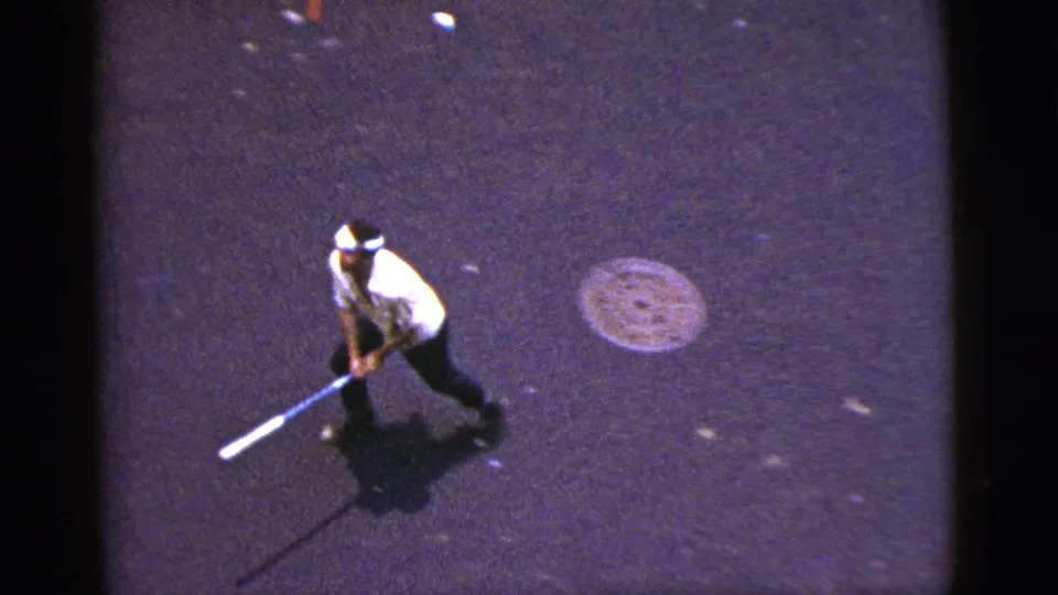 1956 New York City 8mm frame showing a man moving across pavement while holding a long object, seen from above.