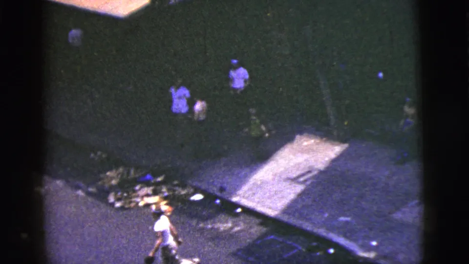 High-angle 8mm frame of pedestrians on a New York City sidewalk with curbside debris in view.