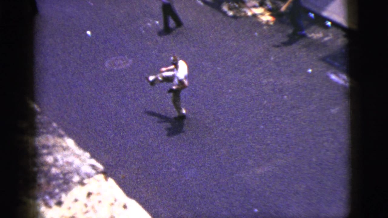 1956 New York City home-movie frame showing a man in a white shirt standing in the roadway during a game of catch.
