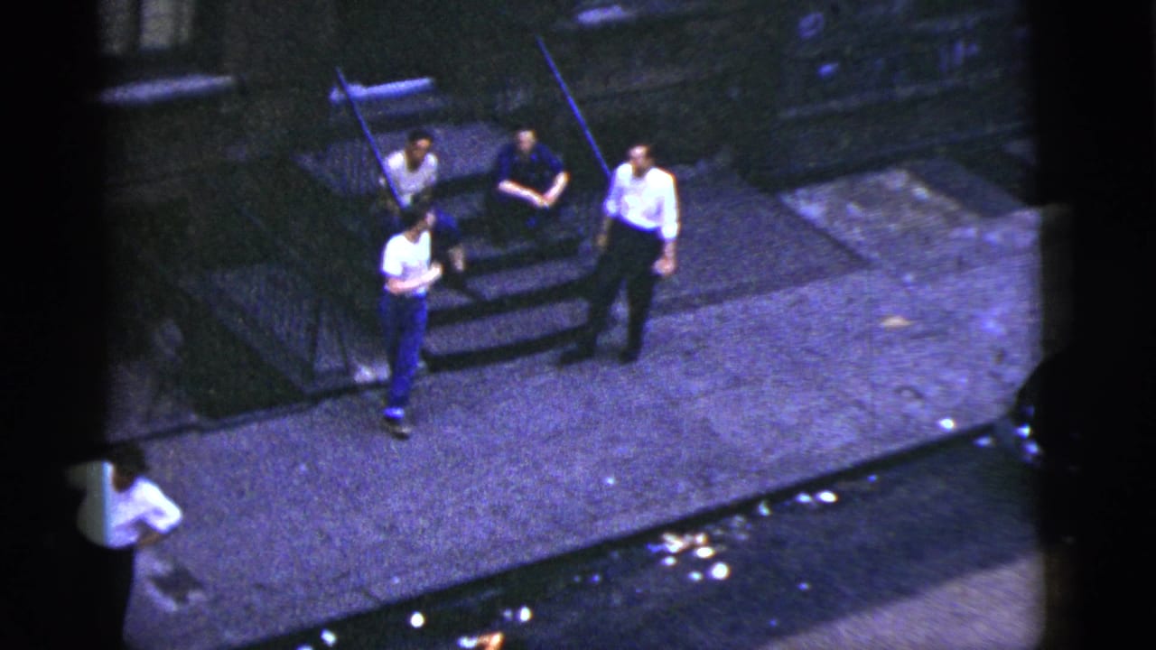 Four young men gather near building steps on a city sidewalk.