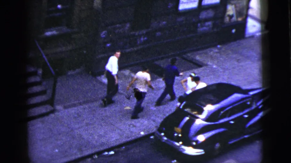 The group continues down the sidewalk toward a dark sedan, filmed from above in 1956 New York City.