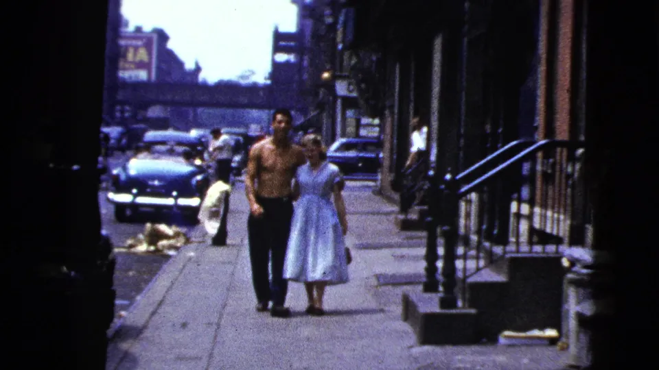 Near the end of the clip, the couple walks toward the camera on a New York City sidewalk with mid-century cars behind them.