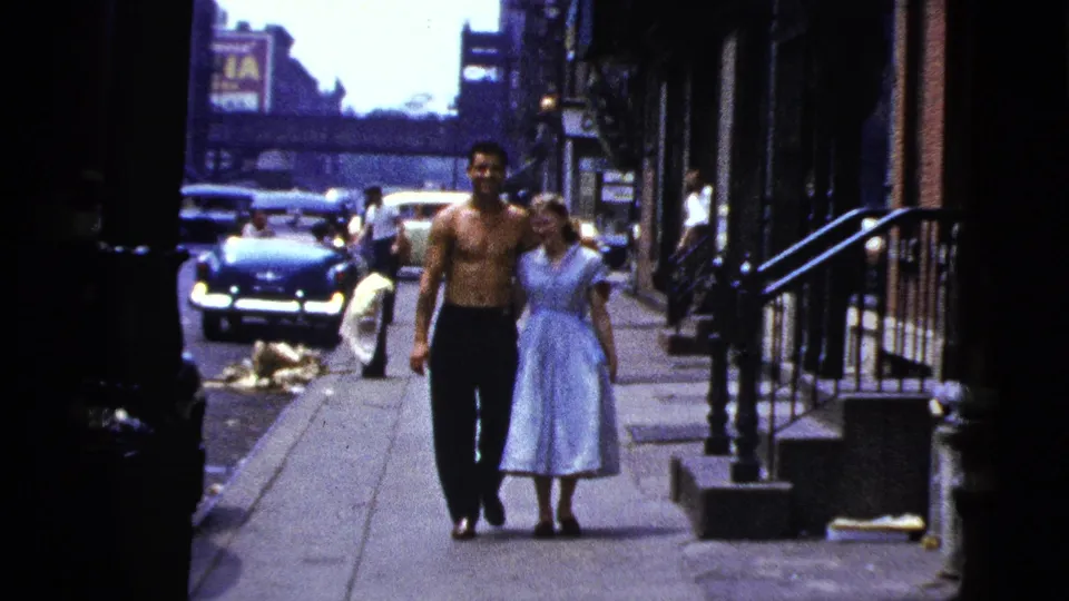 Near the end of the clip, the New York City couple walks toward the lens with vintage cars, stoops, and a distant sign in view.