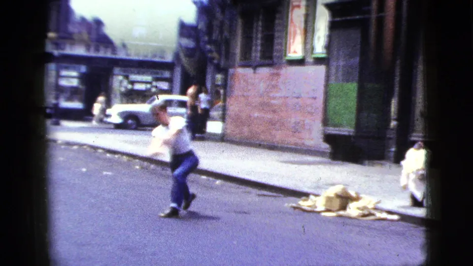 A young man in a white t-shirt runs across the street in the same 1956 New York City home-movie sequence.