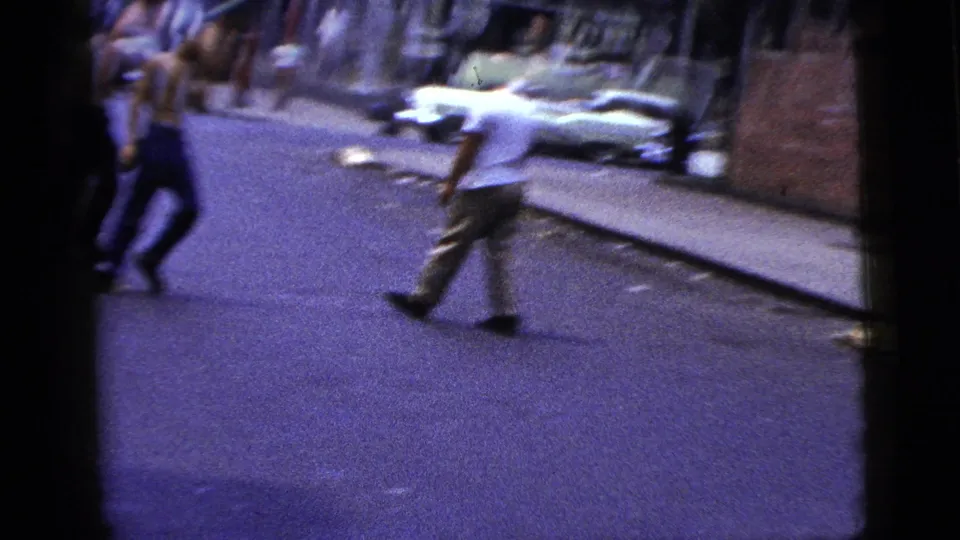 A man carrying a long bar crosses a New York City street in 1956 as other men and pedestrians remain nearby on the pavement and sidewalk.