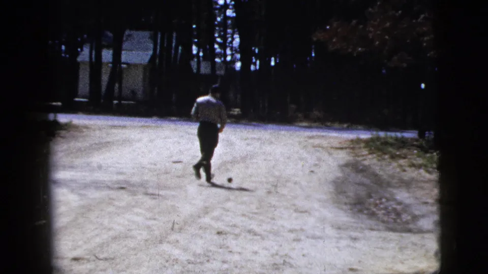The man runs farther down the bright dirt road, with the small ball ahead and trees framing the background in the 1956 New York clip.