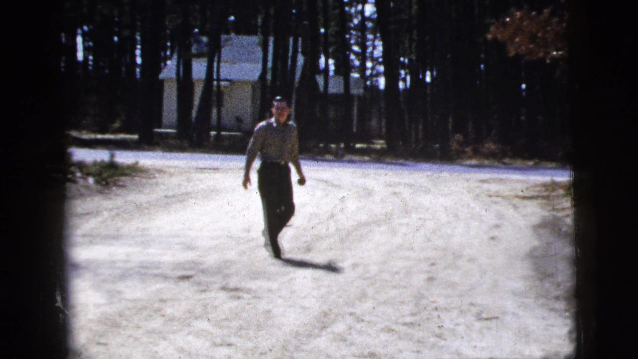 Man walking on a bright dirt road with trees and a small building behind him.