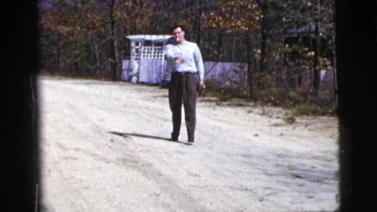 A man in a light shirt stands in the road during a 1956 New York City-labeled home-movie scene of adults playing catch.