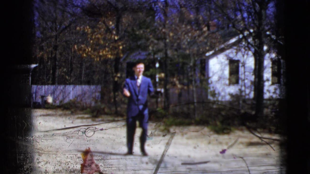 Man in a blue suit faces the camera while holding a glove near a dirt road.