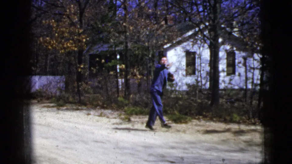 The final frame shows the suited man turning mid-action on the dirt road, with white houses, fencing, and trees behind him.