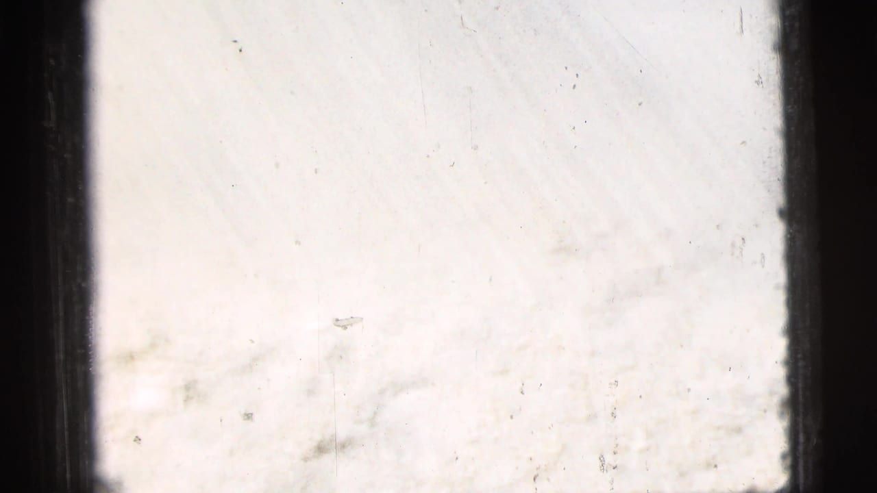 Light-toned 8mm frame from the 1956 New York City clip, showing film edge, faint scratches, and minimal readable subject detail.