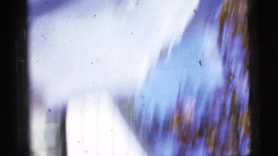 Motion-blurred 8mm frame from the 1956 clip, with blue-purple color shifts, dark borders, and autumn-toned streaks.
