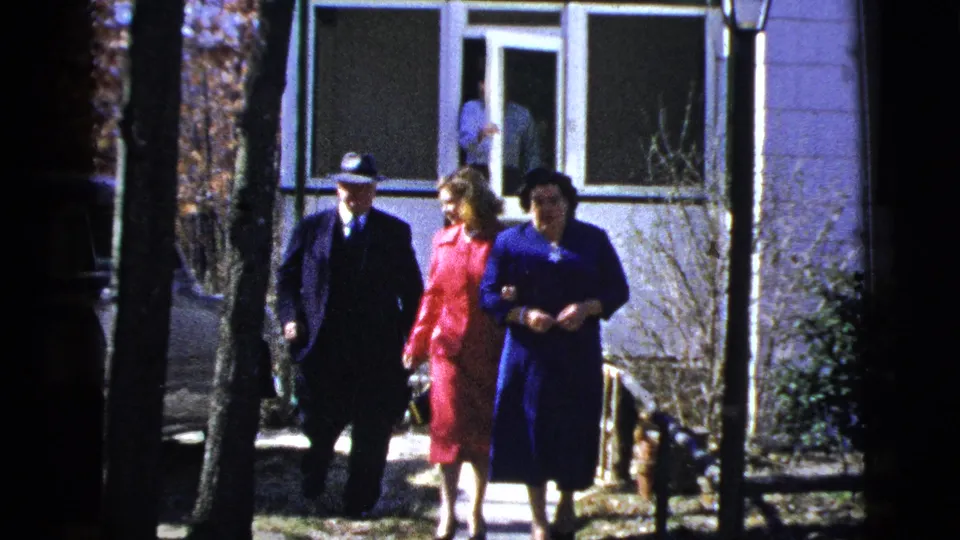 The trio, dressed formally, moves down the walkway past trees and porch railings outside the New York residence.