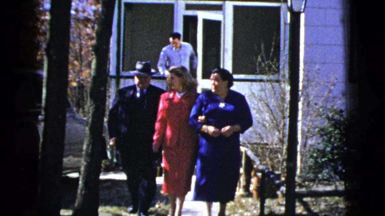 Three dressed adults walk from a house along a tree-lined path.