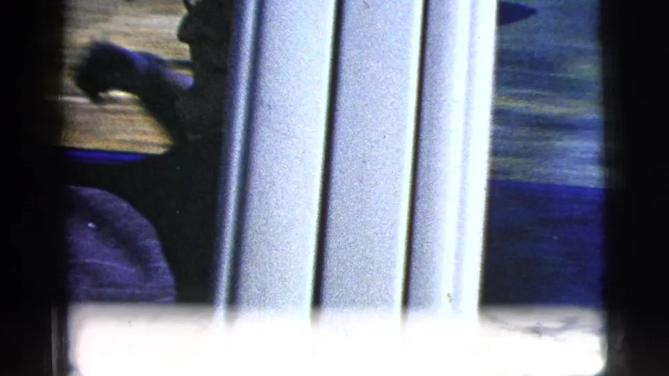 A soft, partially obscured 8mm frame appears to show a person near or inside a car, with strong film gate borders and motion blur.