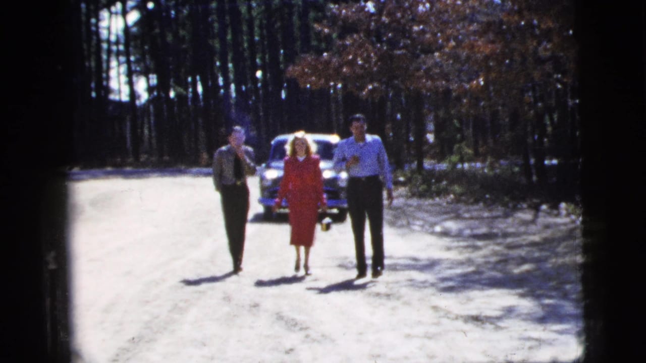 The trio walks closer in 1956 New York City 8mm footage, framed by pine trees and a following car with bright reflections.