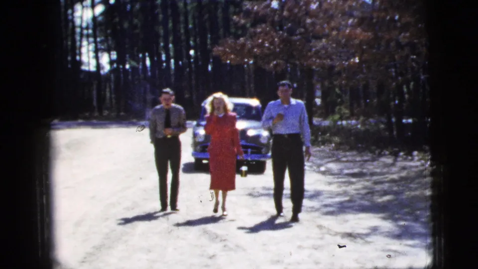 At the end of the 1956 New York City clip, three adults with drinks approach the camera as a vintage car follows behind them.