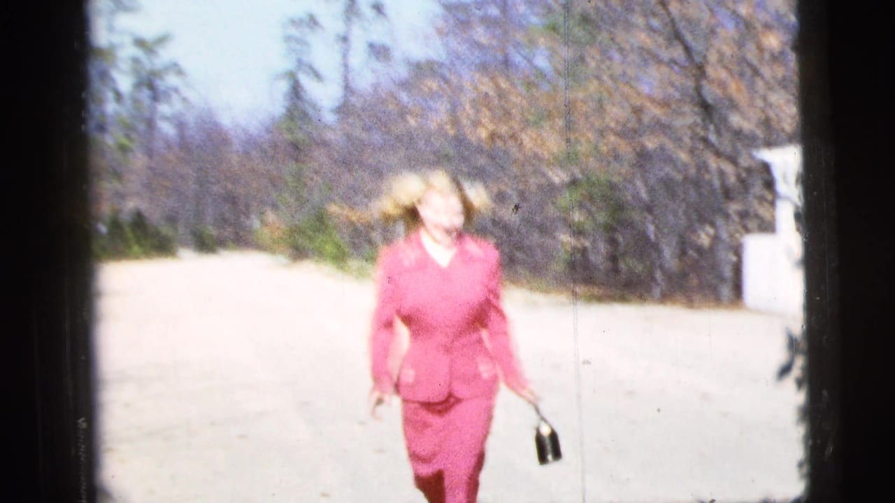 In supported 1956 New York City home-movie footage, a blonde woman in a pink suit approaches on a sunlit road.