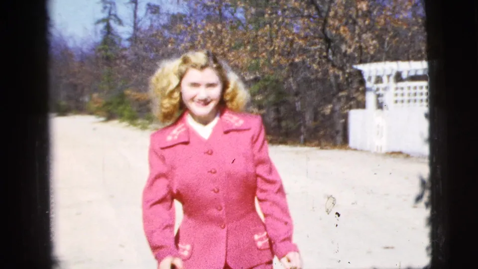 A closer frame shows the woman smiling in a pink suit, with the pale road and white fence receding behind her.