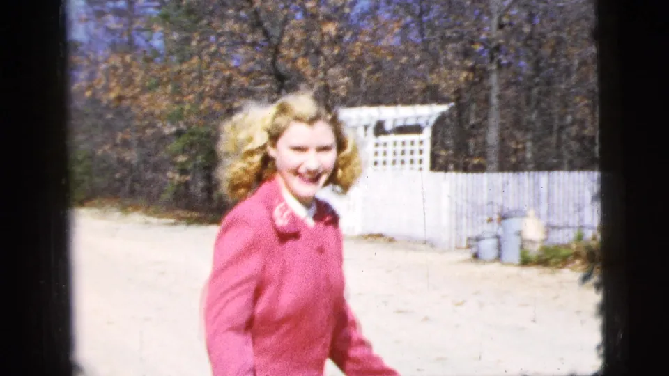 Near the end of the clip, the woman gestures playfully beside the camera with a white fence and roadside objects behind her.