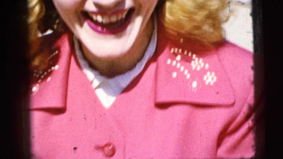 A close, cropped 8mm frame emphasizes the woman’s smile, lipstick, red embroidered coat and white collar.