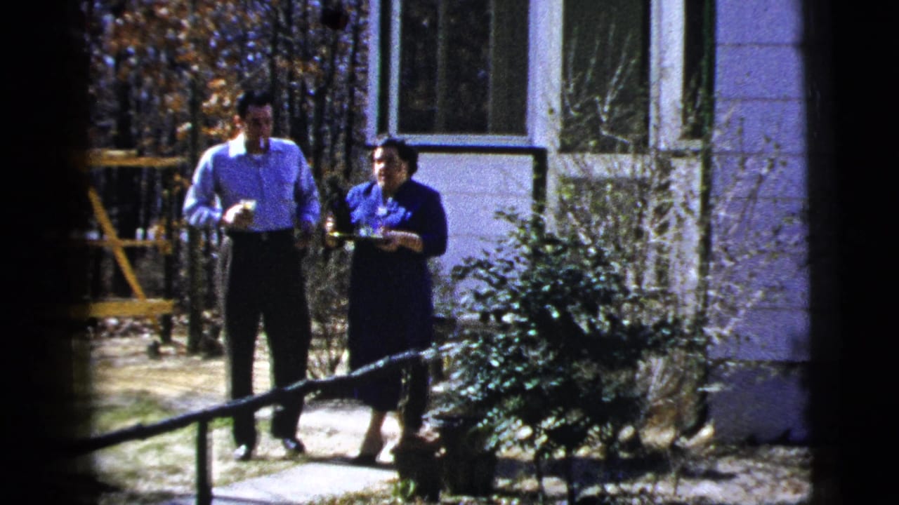 Man and woman stand on a concrete path beside a house outdoors.