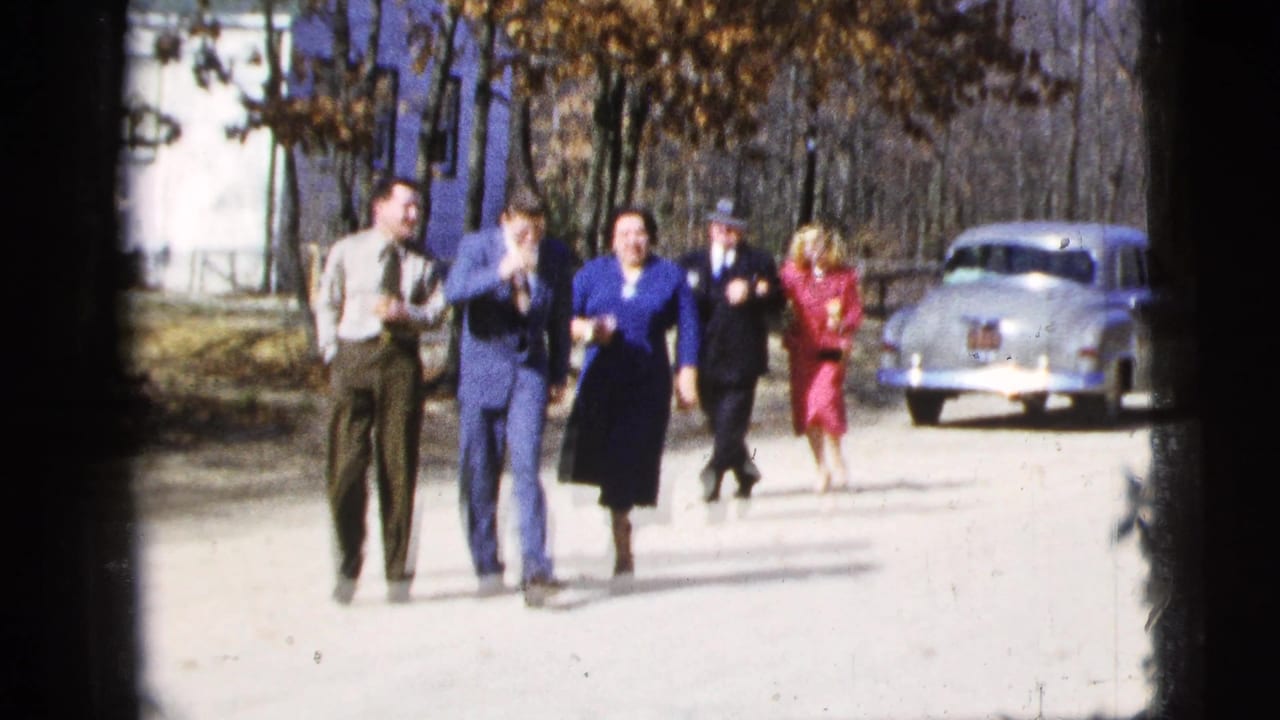 In 1956 New York City home-movie footage, well-dressed adults walk toward the camera on a bright street near a silver sedan.