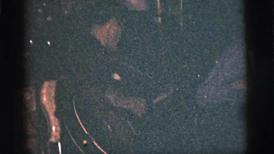 In the low-light 1956 New York City home movie, shadowed people cluster in a dark interior with visible grain and scratches.