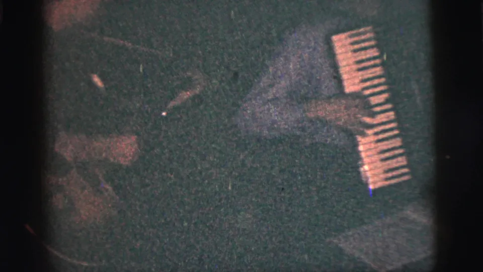 A person appears beside or playing a small keyboard in dark 1956 New York City 8mm footage, with hands and keys partly visible.
