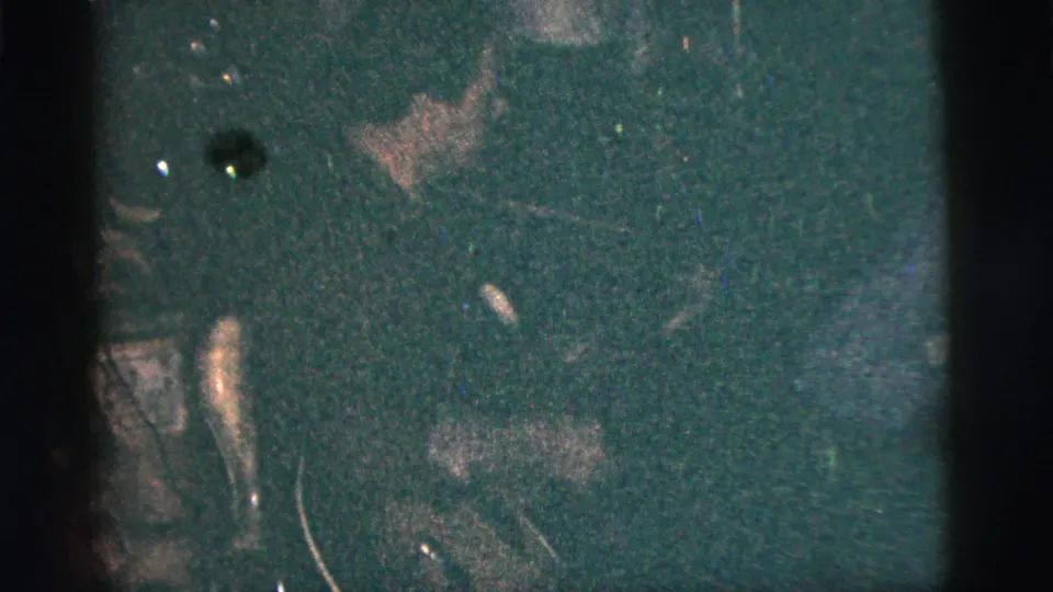 A very dim frame shows indistinct people or room activity, with strong grain and a dark film edge.