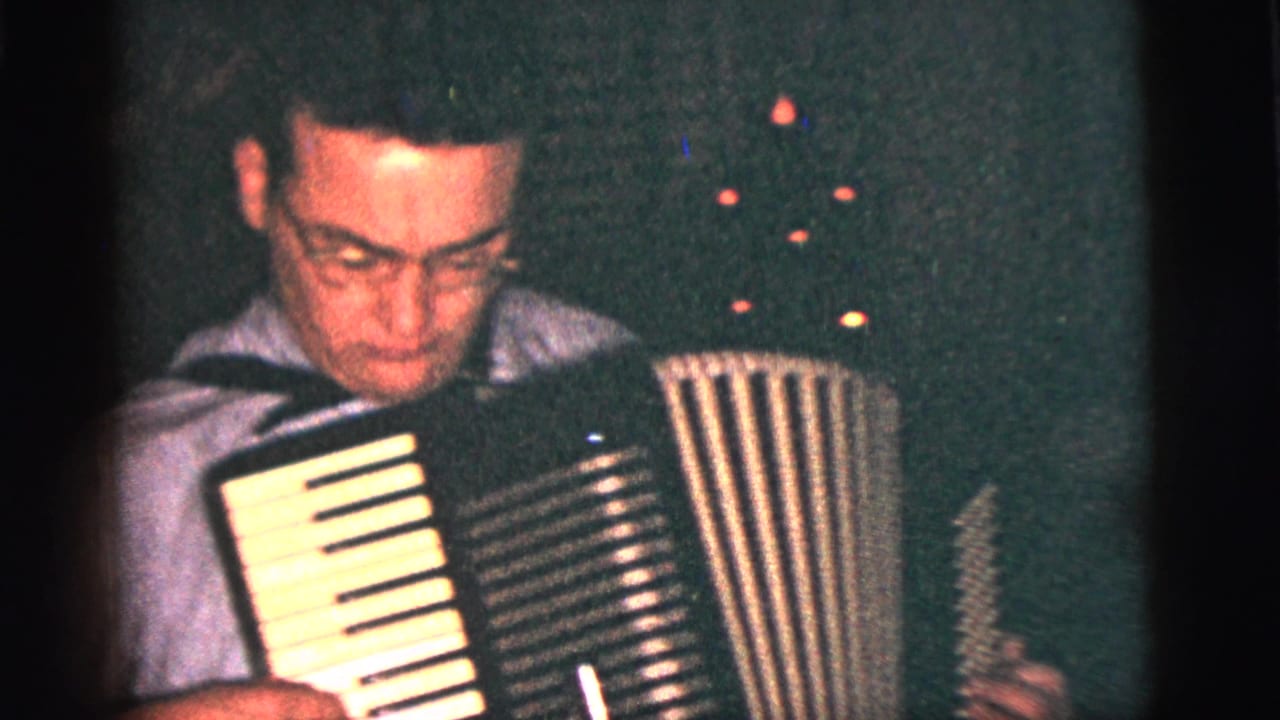 Man in a light shirt plays an accordion in a dim room.