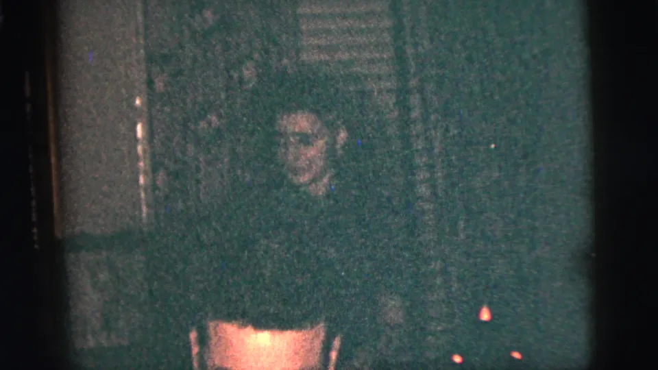 A shadowed onlooker is visible behind the cropped accordion player in this grainy 1956 New York City home-movie frame.