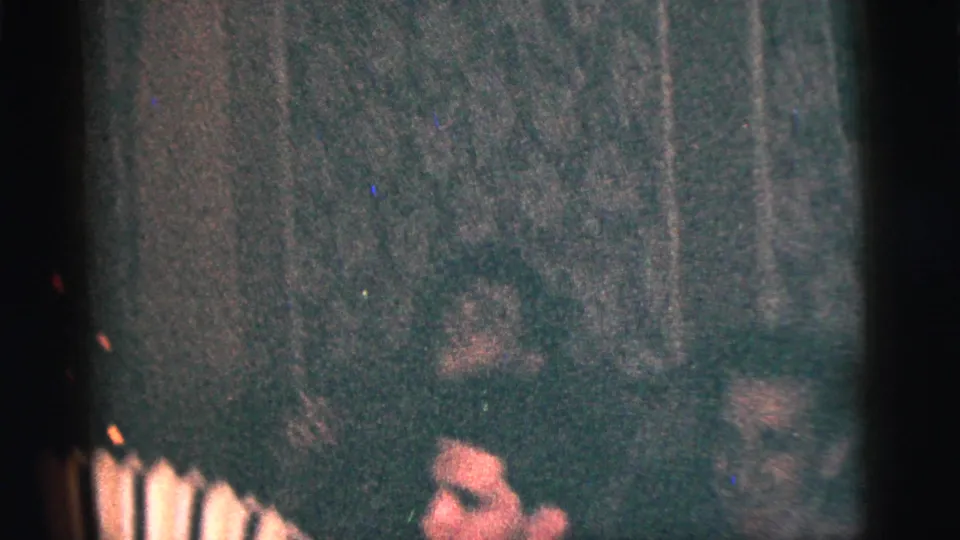1956 New York City home-movie frame of a young man playing a small accordion in a dim private interior with men around him.
