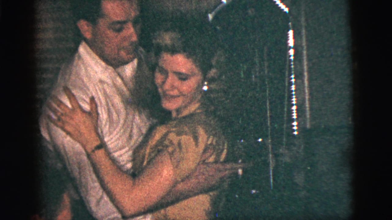 1956 New York City home-movie frame of a man in a white shirt and a woman in a light dress dancing closely indoors.
