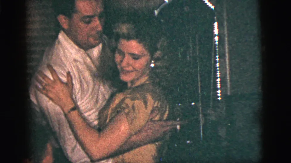 1956 New York City home-movie frame of a man in a white shirt and a woman in a light dress dancing closely indoors.
